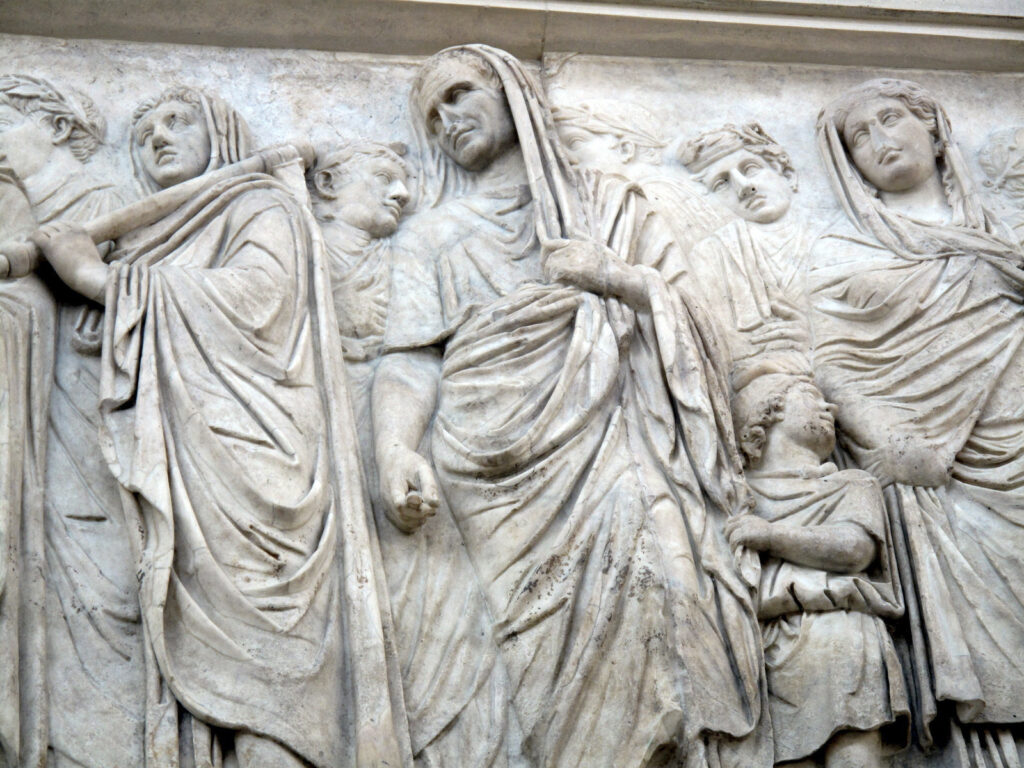 Toga mit Sinus Marcus Vipsanius Agrippa mit über den Kopf gezogener Toga beim Opfer (Fries des Ara Pacis in Rom). Die bauschige Überlappung bzw. Drapierung - das Sinus - diente möglicherweise als Tasche. Von Institute for the Study of the Ancient World - Flickr: Procession on the Ara Pacis (I), CC BY 2.0, https://commons.wikimedia.org/w/index.php?curid=25046441